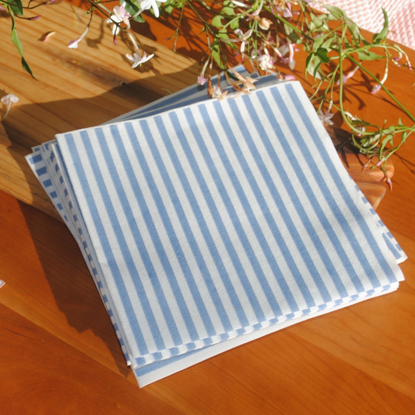 Seersucker paper napkins linen feel disposable luncheon napkins blue and white stripes. Striped napkins close up image where you can see the linen like fabric disposable napkins sit on a wooden table.